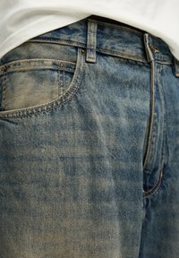 Vaqueros de mezclilla azul desgastados con un corte clásico. Presentan cinco bolsillos, costuras visibles y un cierre de botón en la cintura.