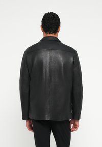 Schwarze Lederjacke mit geradem Schnitt, klassischem Kragen und glatter Oberfläche, ohne sichtbare Verzierungen oder Muster.