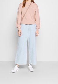 Jasnoróżowy sweter z okrągłym dekoltem, szerokimi rękawami i białym napisem. Połączony z luźnymi, jasnoniebieskimi dżinsami i białymi trampkami.