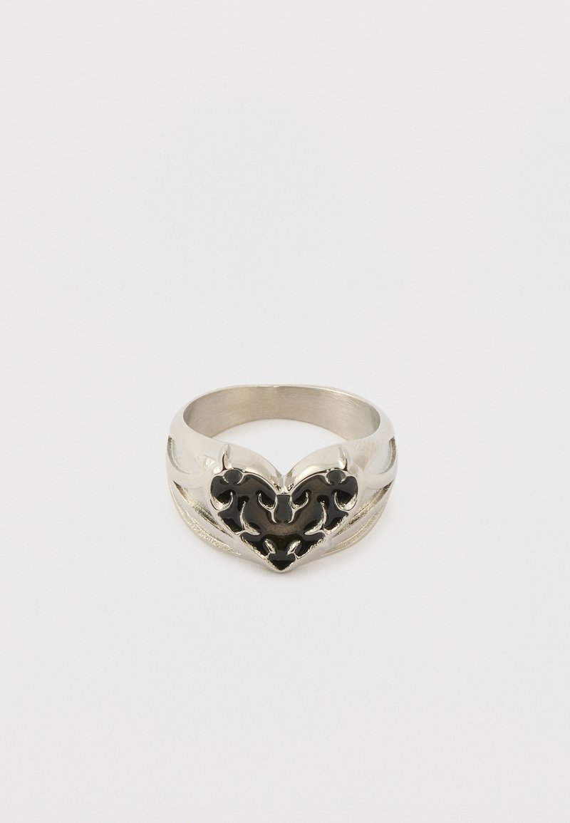 Anillo de plata con un diseño de corazón negro con patrones intrincados recortados sobre un fondo blanco liso.