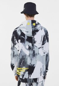 Felpa con cappuccio con motivo astratto in nero, bianco e grigio, caratterizzata da accenti gialli e testo sul retro. Misto cotone, vestibilità comoda.