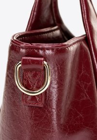 Bordeaux leren handtas met een getextureerd oppervlak, een goudkleurige metalen hardware ring en een gestructureerde bovenopening.