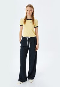 Camiseta amarilla de manga corta con ribete marino y gráfico, combinada con pantalones anchos marinos con cintura ajustable. Zapatillas blancas.