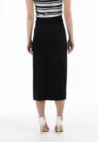 Midu rok hitam bertekstur dengan pinggang yang pas dan sedikit belahan di belakang, dipadukan dengan sandal hak tinggi putih.