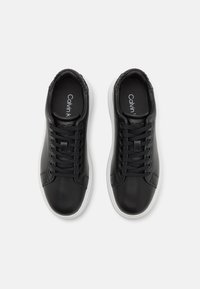 Adidași negri din piele cu tălpi de cauciuc alb, având vârful rotund, design cu șireturi și accente texturate negre pe guler.