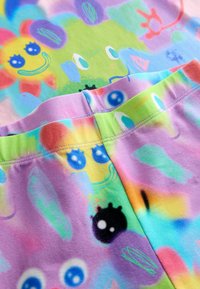 Bunt gemusterter Stoff mit lächelnder Sonne, abstrakten Augen und verspielten Formen in sanften Farbtönen von Lila, Grün, Gelb und Blau, die zusammen genäht sind.
