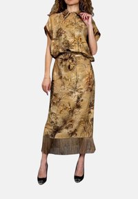 Completo due pezzi color sabbia con una blusa a maniche corte ampia e una gonna lunga. Presenta una stampa floreale e frange all'orlo.