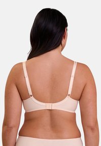 Bra beige con textura suave, con correas ajustables, cierre de gancho y ojal, y borde ondulado en la banda. Vista trasera.