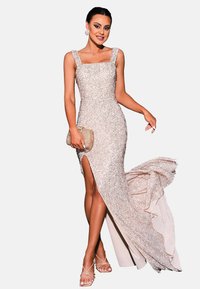 Glitterend avondjurk in lichtroze met een vierkante halslijn, een zijsplit en een vloeiende achterkant. Gecombineerd met een transparante clutch en sandaaltjes.