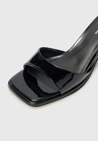 Black patent leather open-toe sandal with wide crossed straps, square toe design, smooth texture, and low heel.
