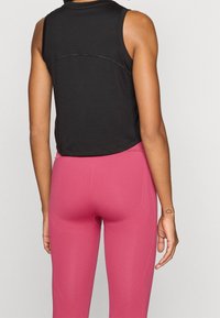Czarny bezrękawnik z zaokrąglonym dołem, zestawiony z różowymi dopasowanymi legginsami o gładkiej teksturze i teksturowanych szwach.
