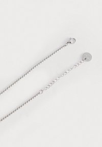 Collana in argento con chiusura a gancio, caratterizzata da un design a maglia testurizzata e un piccolo tag circolare con il nome del marchio.