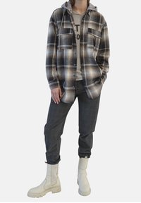 Rutig overskjorta i svart och beige med en grå huva, bärs över en ljusgrå sweatshirt och mörka rutig byxor, kompletterat med vita stövlar.