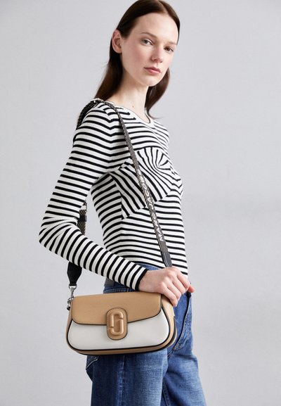 Crossbody bag with a tan and white leather design, featuring a rounded shape, top flap, and a branded hardware detail on the front.