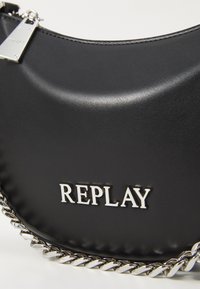 Bolso sintético negro con textura suave, que presenta detalles en cadena plateada y el logo grabado "REPLAY" en la parte frontal.