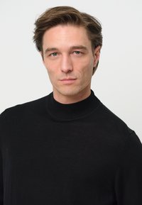 Svart polotröja i finstickad kvalitet. Slät textur, åtsittande design, med hög krage och minimalistisk stil.