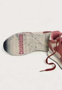 Sneakersula med en detaljerad kartdesign och texten "Castelbonga", bredvid en rosa och beige sko med lösa röda snören på vit bakgrund.