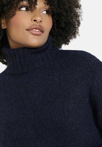 Tumši zili turtlenecks džemperis ar tekstūru. Mīksts, adīts audums ar ribotu apkakli un smalku spīdumu, radīts siltumam.