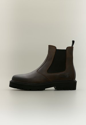 Botte Chelsea en cuir marron avec panneau latéral élastique noir, semelle épaisse noire et languette à l'arrière, sur fond neutre.