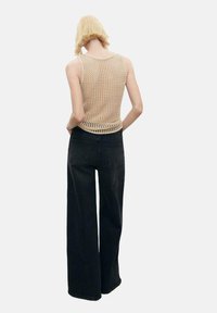 Knit beige tank top with open weave, paired with high-waisted black wide-leg jeans. The outfit features clean lines and minimal detailing.