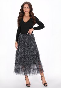 Sort langærmet top kombineret med en lagdelt sort og grå leopardprint tulle nederdel. Modellen bærer sorte stropbehag.