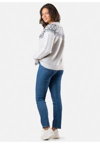 Pullover grigio in maglia con un motivo color blu scuro sulla parte superiore, abbinato a jeans blu e scarpe da ginnastica bianche. Tessuto morbido, vestibilità casual.