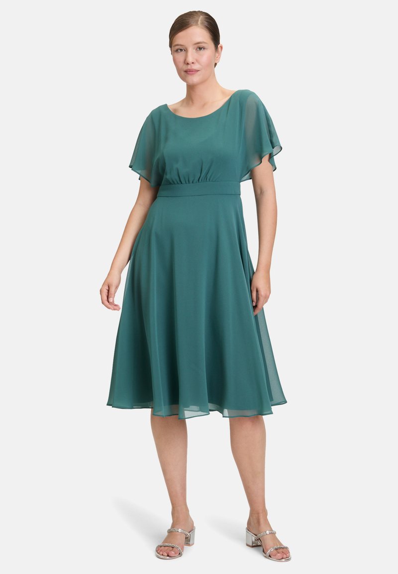 Türkisfarbendes Chiffonkleid mit kurzen, fließenden Ärmeln, gerafftem Taillenbereich und ausgestellt Rock, kombiniert mit silbernen Absatzsandalen.