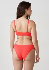 Rotes Bikini-Set mit nahtlosem Bralette und tief sitzenden Slips. Glatte Textur, verstellbare Träger und minimalistisches Design.