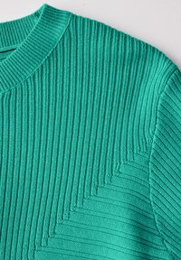 Tyrkysový pletený svetr s vertikální žebrovanou texturou, kulatým výstřihem a cikcak vzorem podél ramene a rukávu.