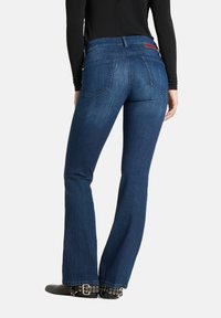 Ciemnoniebieskie dzwony z średnim stanem, z tylnymi kieszeniami i czerwoną metką na pasku, noszone z czarnymi, ćwiekowanymi botkami za kostkę.