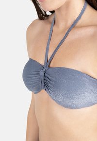 Haut de bikini gris sans bretelles avec tissu froncé et un détail noué au centre. Texture lisse avec un léger éclat dû à des fils métalliques.