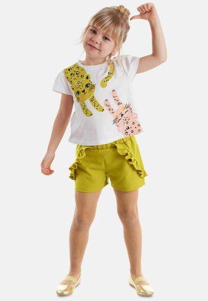 Camiseta blanca con estampados de leopardo/conejo en amarillo y rosa, combinada con pantalones cortos de lima texturizados que presentan volantes. Zapatos planos dorados completan el conjunto.