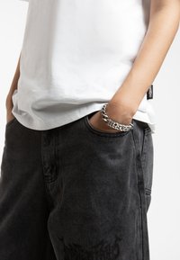 T-shirt bianco in cotone abbinato a pantaloni corti in denim neri. I pantaloni corti presentano una tasca visibile e un delicato dettaglio grafico nero. Accessorio con bracciale in argento.