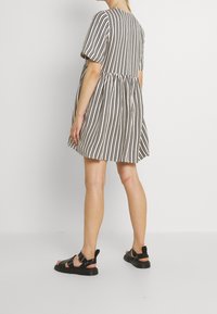 Vestido de manga corta a rayas con cintura plisada, que presenta rayas verticales en blanco y negro. Combinado con sandalias negras de diseño minimalista.