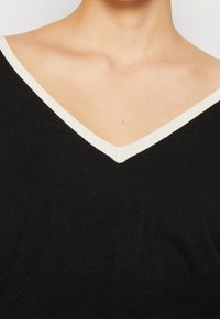 Gros plan sur une personne portant un pull en V noir avec un liseré blanc le long de l'encolure.