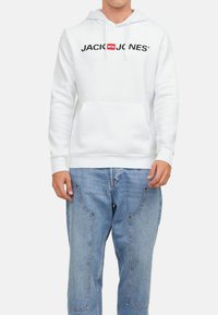 Valkoinen huppuhaalari, jossa on musta "JACK & JONES" -logo rinnassa. Hupparissa on etupuolella kengurutasku ja säätönyöri hupussa.