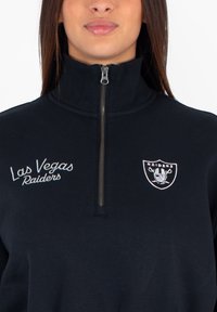 Felpa nera con zip, caratterizzata da ricami dei Las Vegas Raiders sul lato sinistro del petto e un logo dei Raiders sulla destra, realizzata in un tessuto morbido.