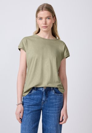 T-shirt verde oliva a maniche corte in un fit rilassato, realizzato in tessuto morbido, abbinato a jeans blu a vita alta, con una texture liscia e un design minimale.