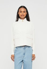 Jaqueta branca quiltada cropped com gola alta, fecho �éclair frontal e dois grandes bolsos no peito. Possui uma textura suave e detalhes em metal dourado.