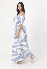 Abito maxi off-the-shoulder blu e bianco con un motivo ondulato, vita arricciata e maniche a palloncino corte. Visibili tacchi a stiletto.