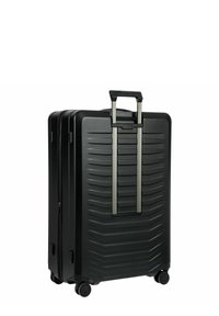 Valigia rigida nera con texture a coste, manico telescopico, quattro ruote e chiusura con doppia cerniera. Gli accenti includono un manico metallico.