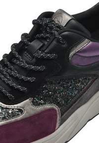 Sneaker nera con glitter nero testurizzato, accenti viola e grigi, e dettagli metallici. Presenta lacci decorati e una suola imbottita.
