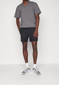 Šedá tričko s krátkým rukávem a výstřihem, spárované s černými šortkami. Bílé a námořnické sportovní boty s limetkovými akcenty. Hladké textury.