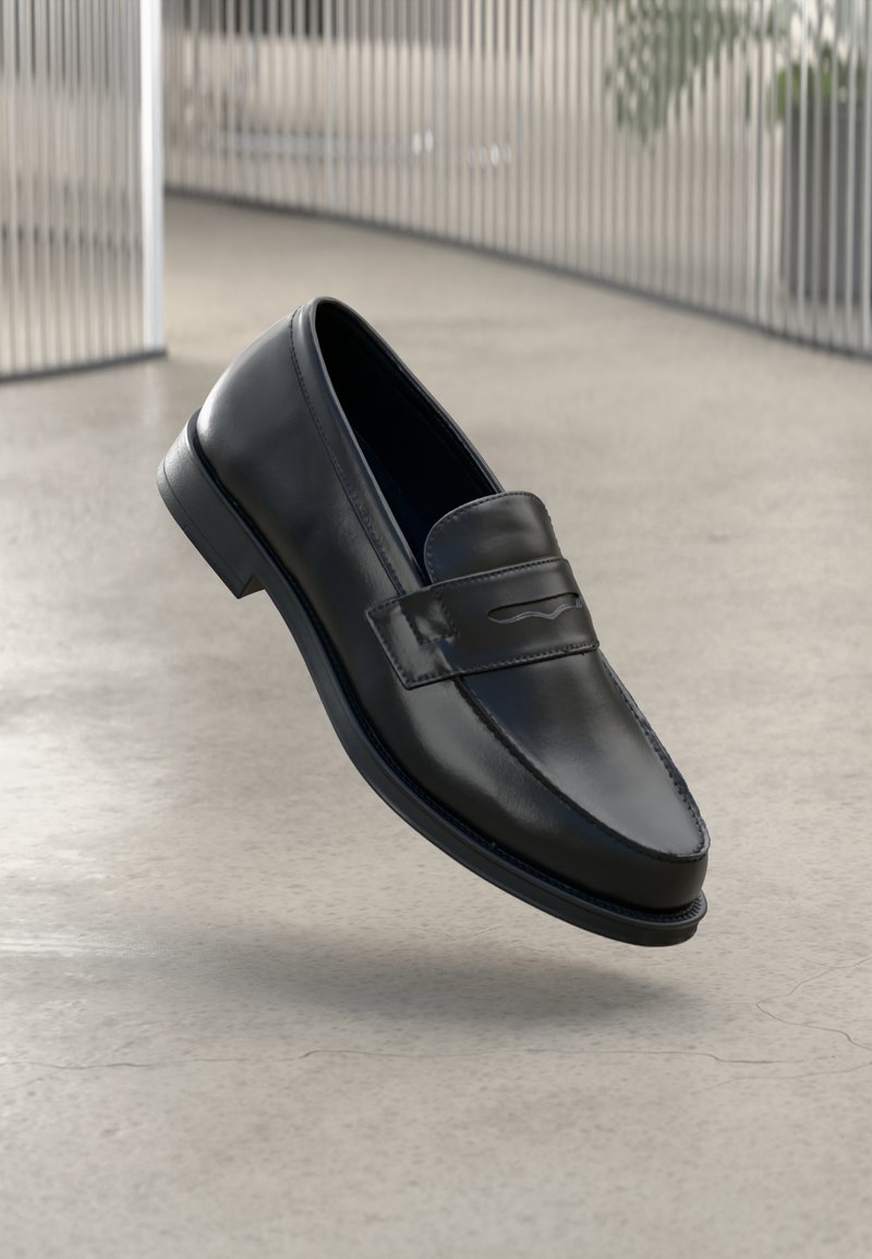 Chaussure mocassin noire en cuir pour homme flottant au-dessus d'un sol en béton lisse gris clair avec des barres métalliques verticales en arrière-plan.
