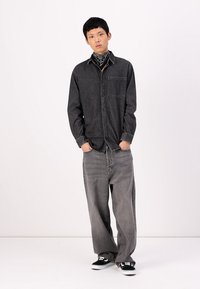Gray denim button-up shirt with a pocket, paired with wide-leg gray jeans. Black sneakers and a black bandana around the neck.