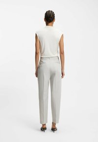 Lichtbeige mouwloos top met een zachte textuur, gecombineerd met op maat gemaakte lichtgrijze broek. De outfit wordt compleet gemaakt met zwarte hoge hakken.