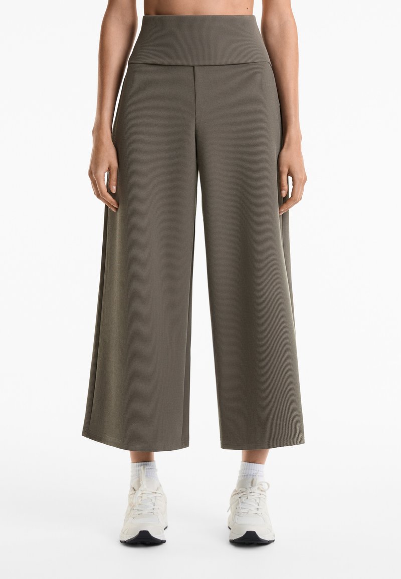 Weite Hose aus geripptem Material, dunkelolivgrün, mit hohem Bund, knöchellang, kombiniert mit weißen Sneakern und Crew-Socken.