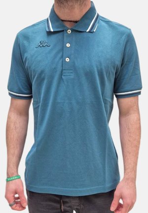 Uomo che indossa una polo blu con colletto e polsini bianchi a righe, tre bottoni e un piccolo logo sul petto.