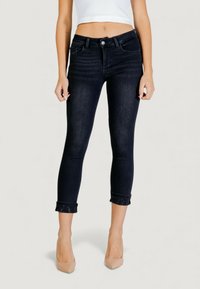 Jeans cropped in denim scuro con una silhouette sagomata, orli risvoltati decorati con piccoli borchie e chiusura classica con bottone in vita.