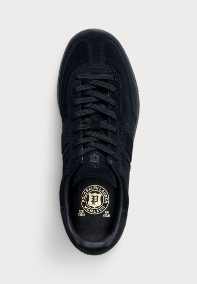 Črne semiš športne copate z okroglo konico, s čipkastim dizajnom, kontrastnimi teksturami in okroglo logotipno nalepko na jeziku.